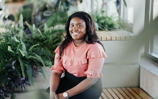 Female student sitting on bench smiling surrounded by plants