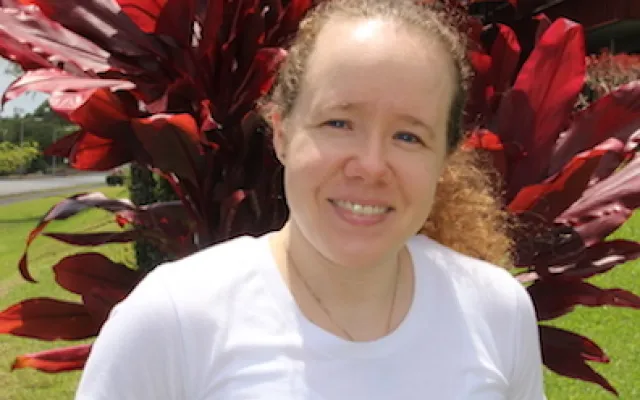 A woman in a white t-shirt standing in front of red shrubbery